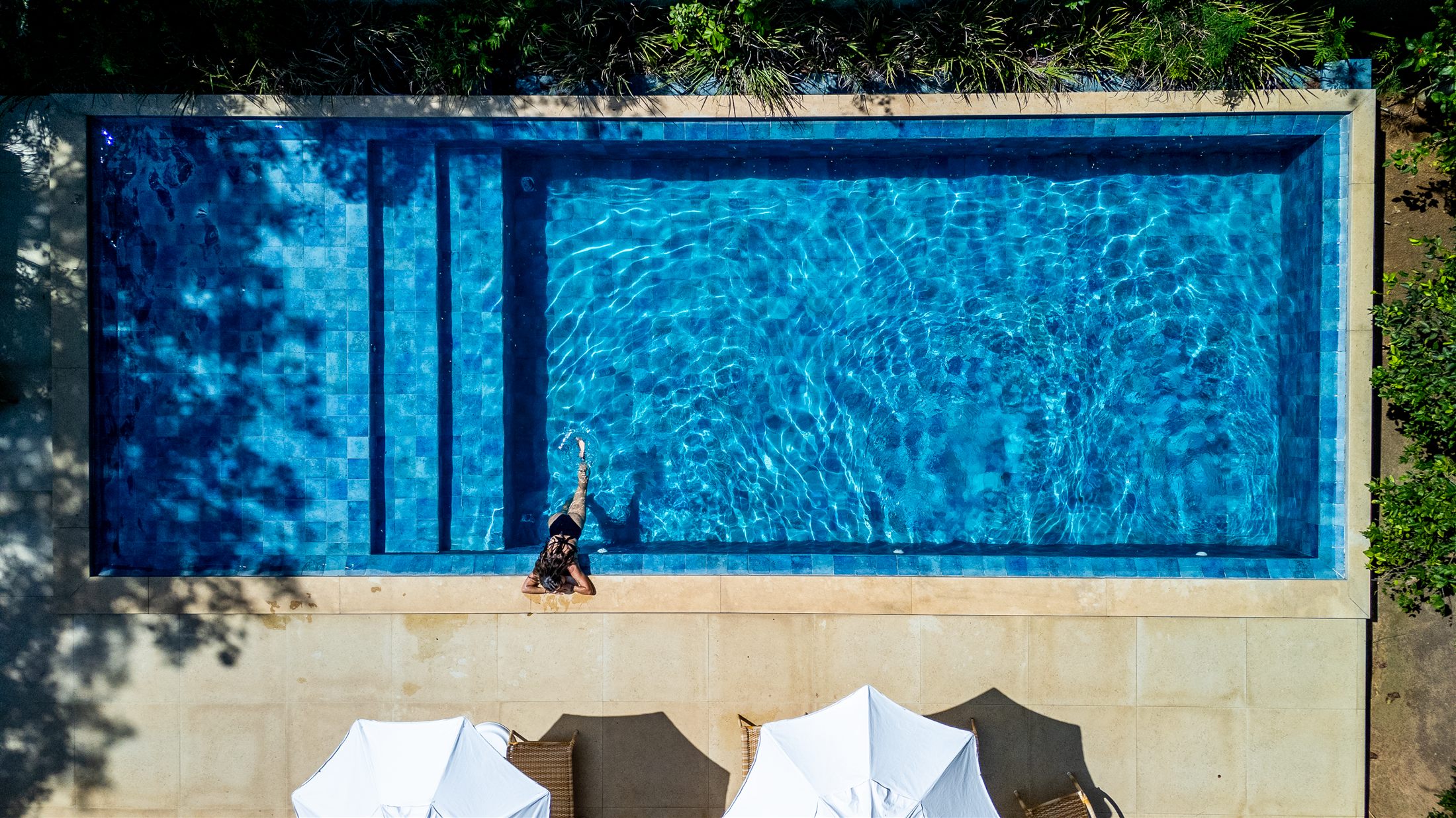 Vista aérea da piscina azul da Pousada Vila Pitanga em Búzios com hóspede relaxando na borda